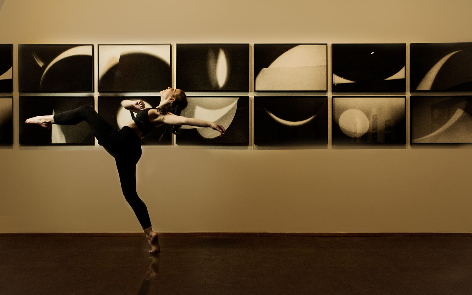 dancer takes an enormous step with back and arm arched back while passing a row of black and white abstract photos