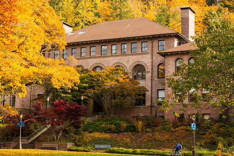 a classical brick building with tiled roof framed by trees in fall foliage