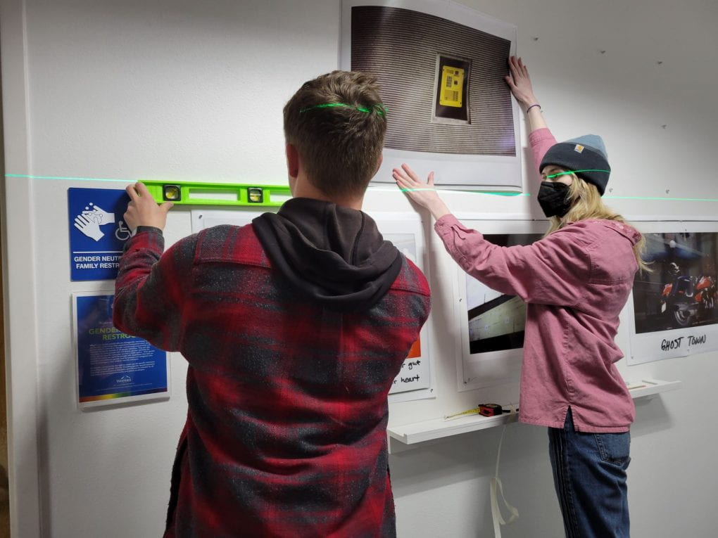 Students using a laser level guide to hang large photos on a wall