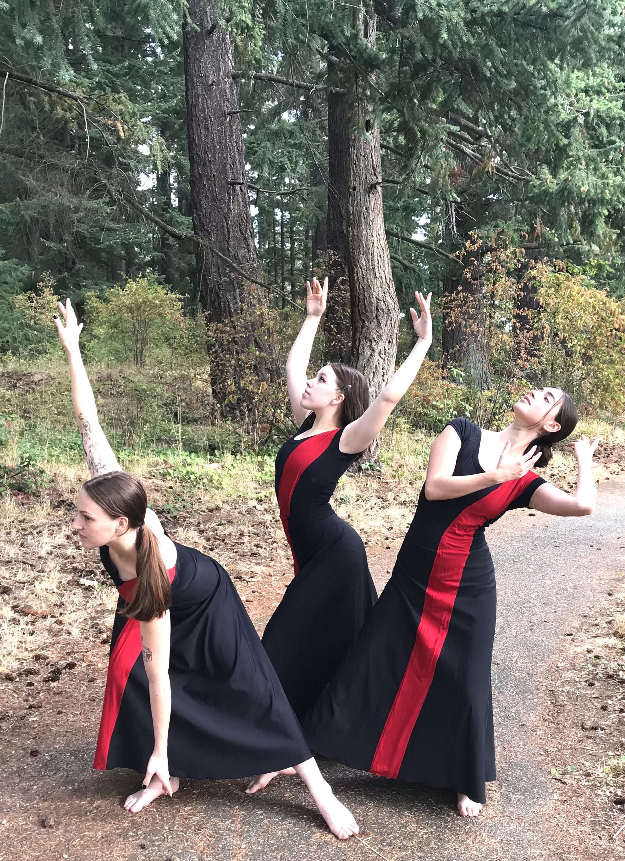Three dancers in matching dresses strike unique poses together in the woods