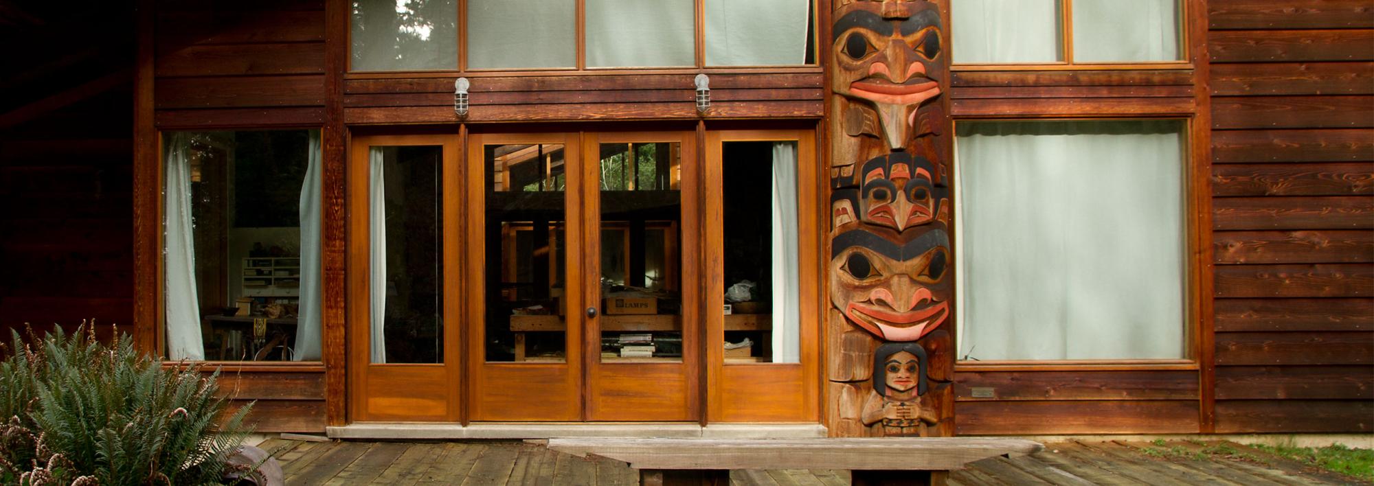 front of a rustic gallery building with glass doors and carved totems