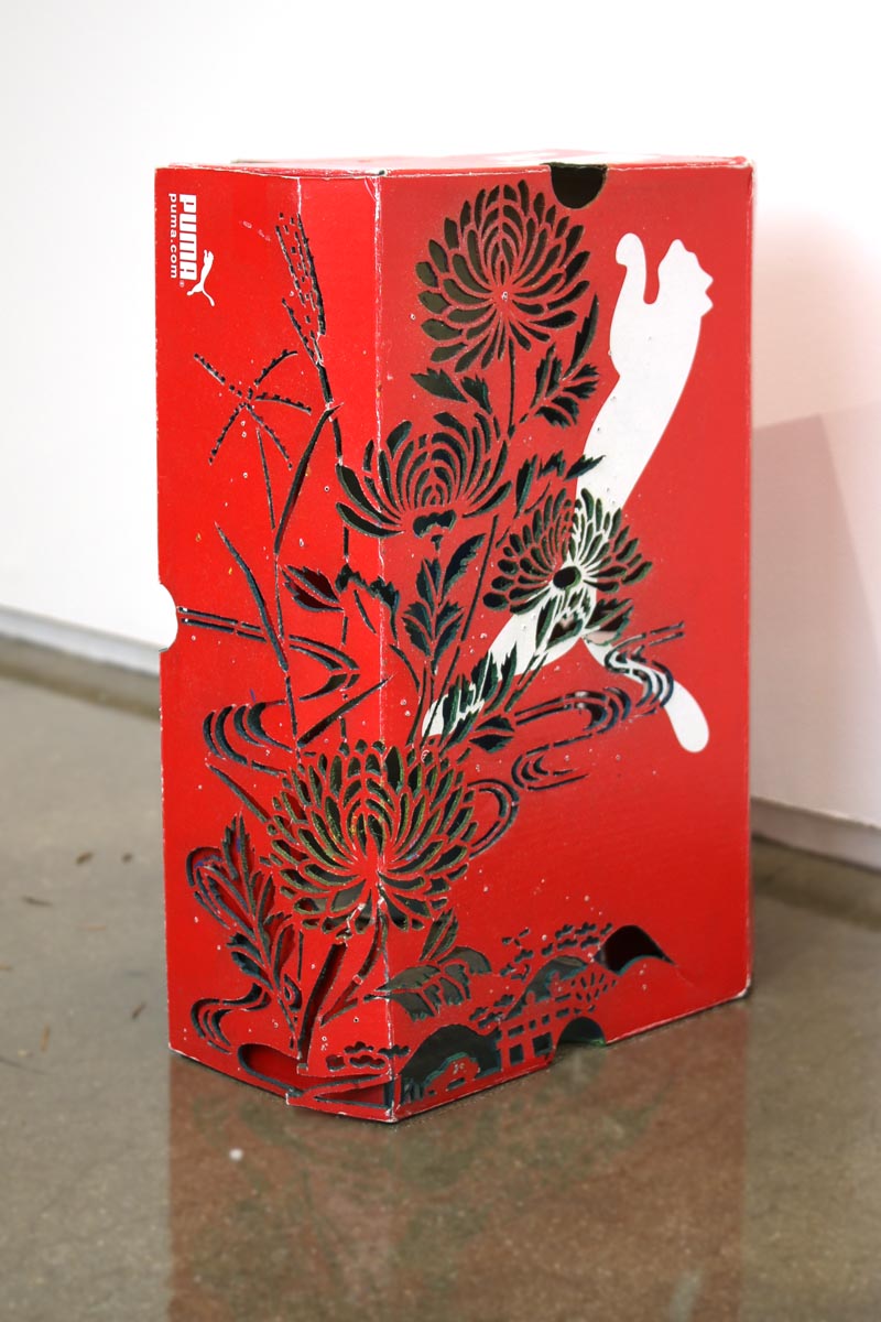 a red shoe box with the Puma brand logo, over which is painted a floral design in black.