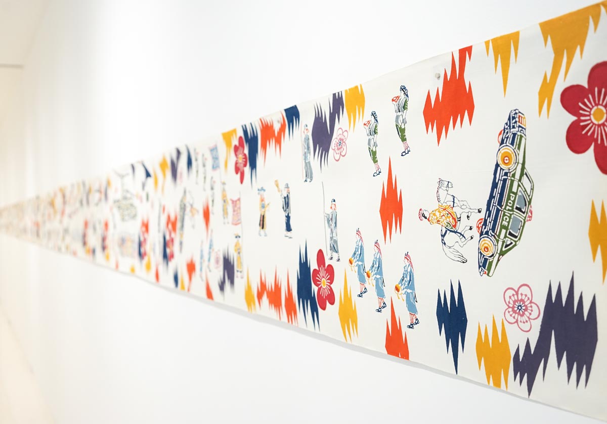 a very long strip of fabric or paper colored with bright splashes of primary colors and tubmling illustrations of cars.