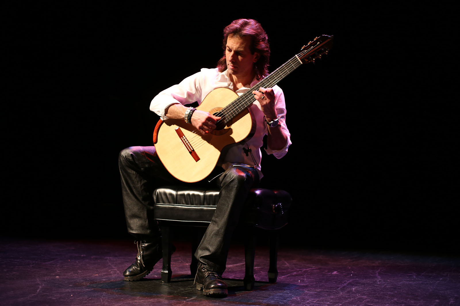 a person playing a guitar sits in a pool of light on a dark stage