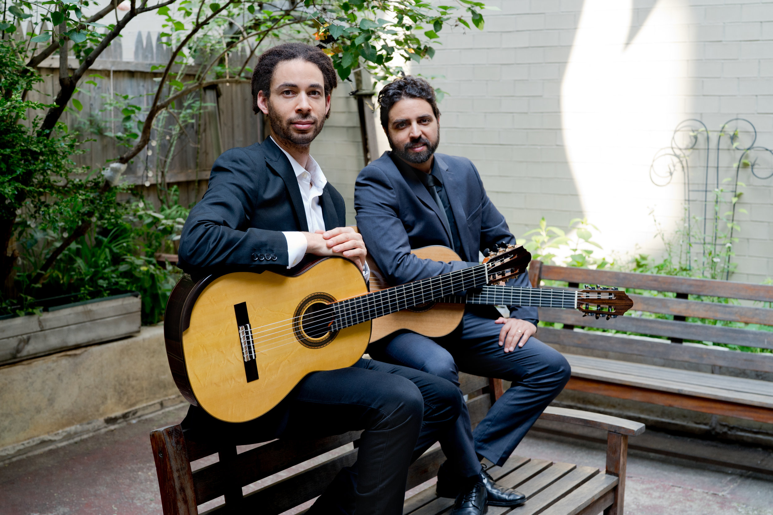two bearded people on a bench with guitars