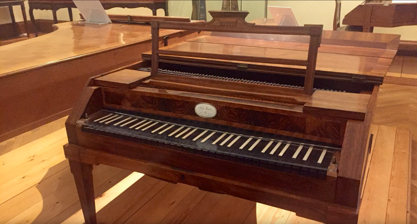 a fortepiano sits on a wood floor surrounded by other kinds of pianos