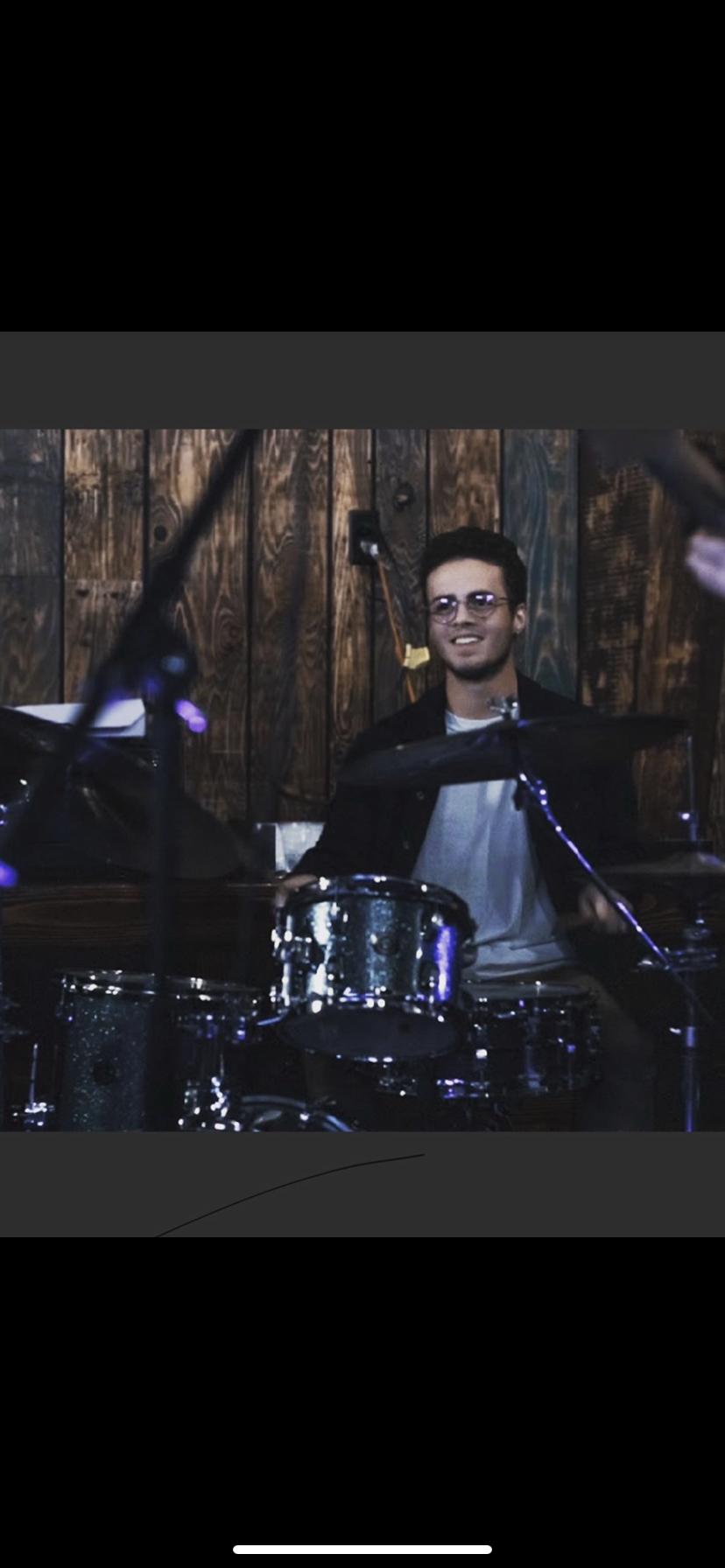 A happy person playing drums in front of a wood paneled wall