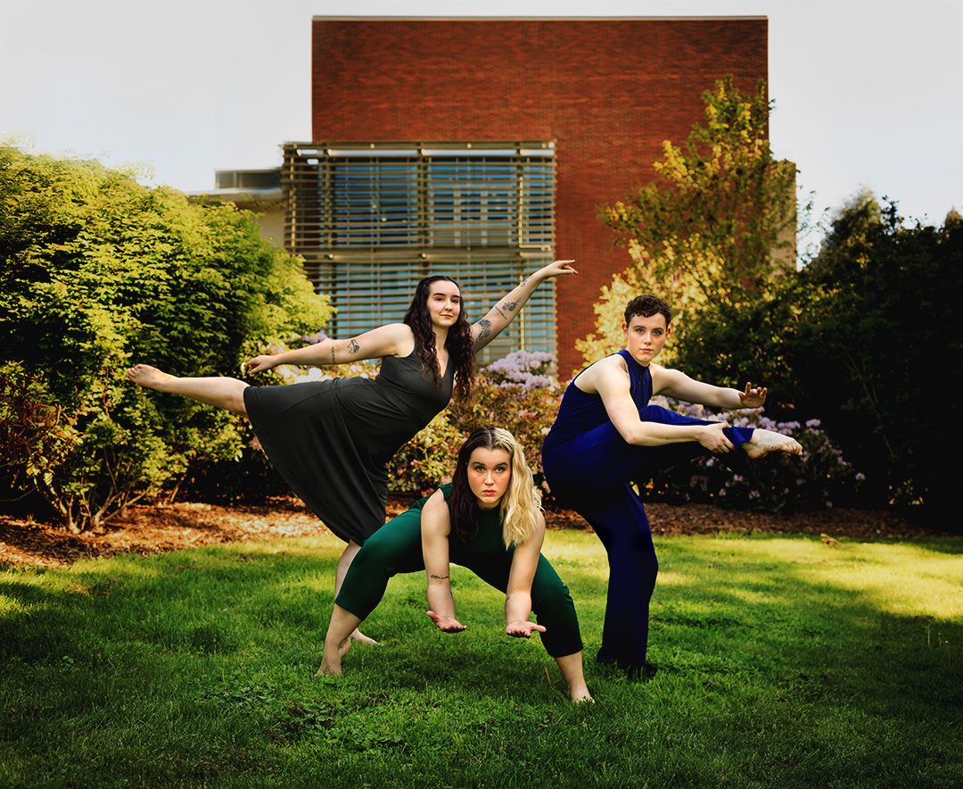 3 dancers in athletic poses in an evening-lit garden. One squatting, the others stand with a foot pointed outward.