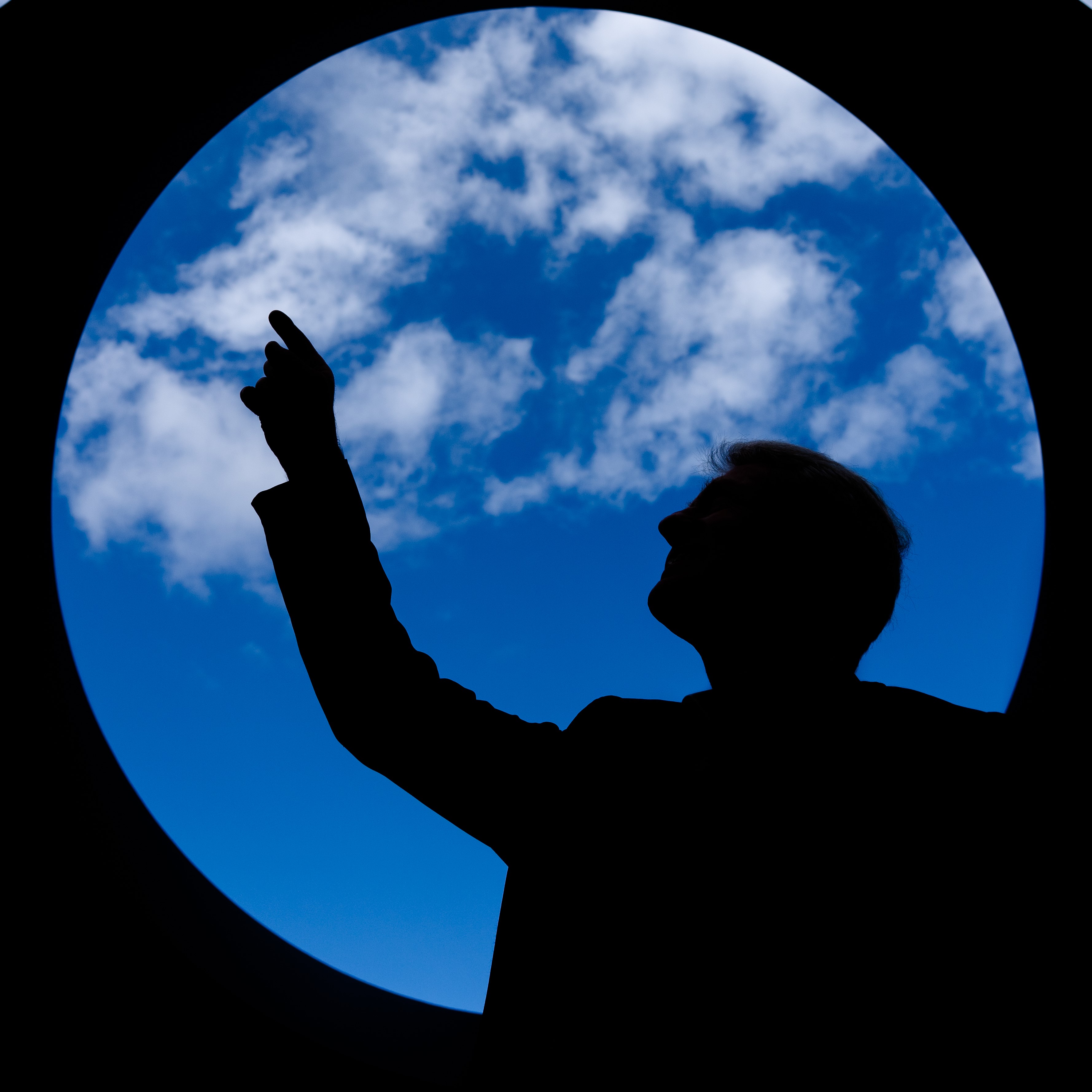 silhoutte of a person pointing up at clouds in a blue sky from inside a circle