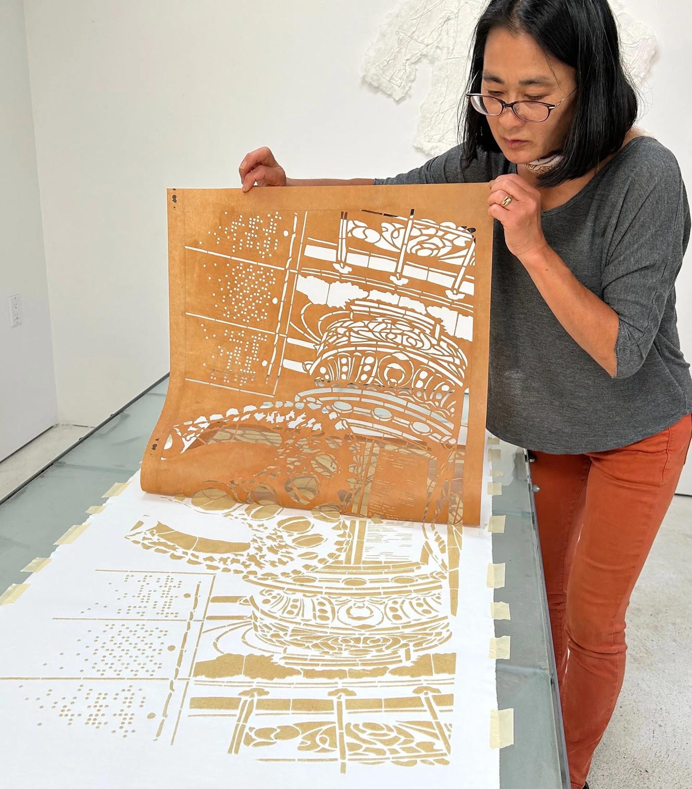 an artist lifts a thin stencil from a piece of fabric on a table