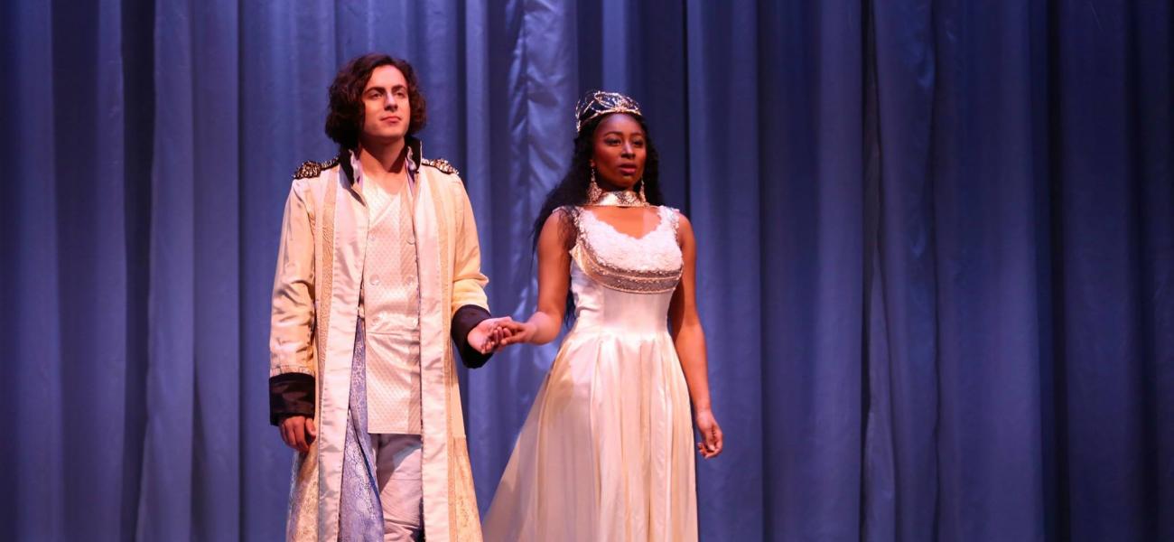 Two opera singers holding hands wearing white garb on stage