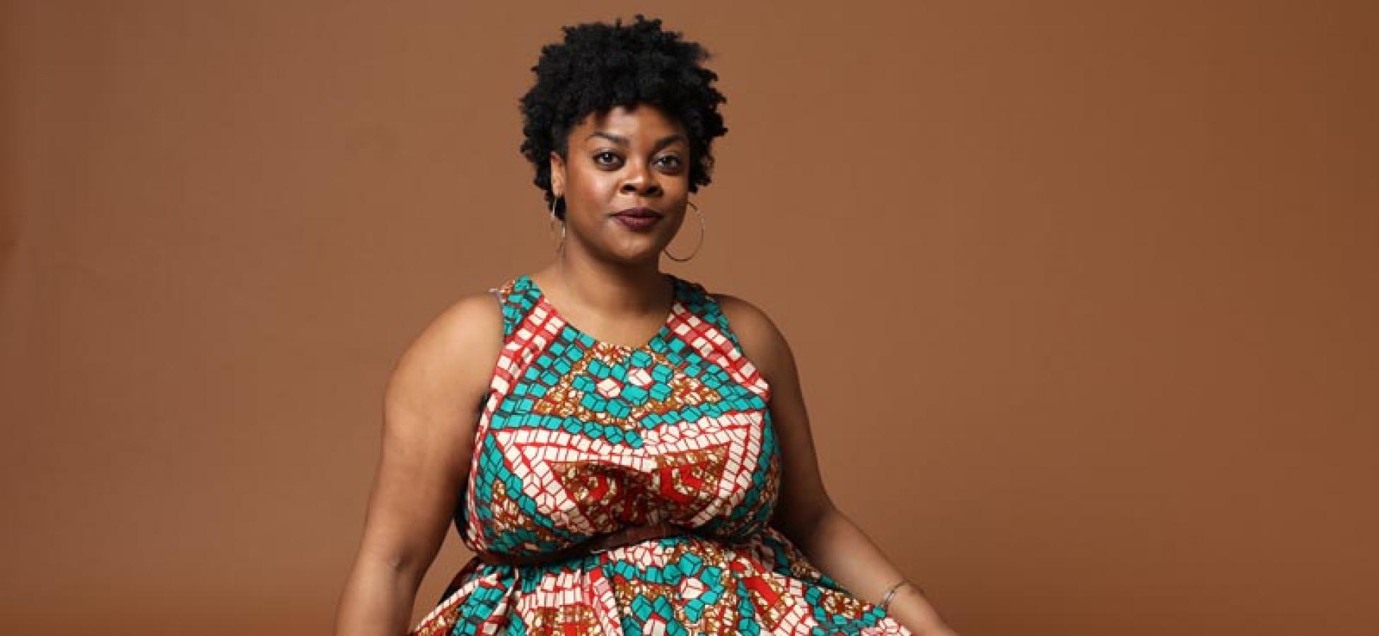 Rashawn Nadine Scott sits on the floor in a patterned sleeveless dress looking comfortable and confident