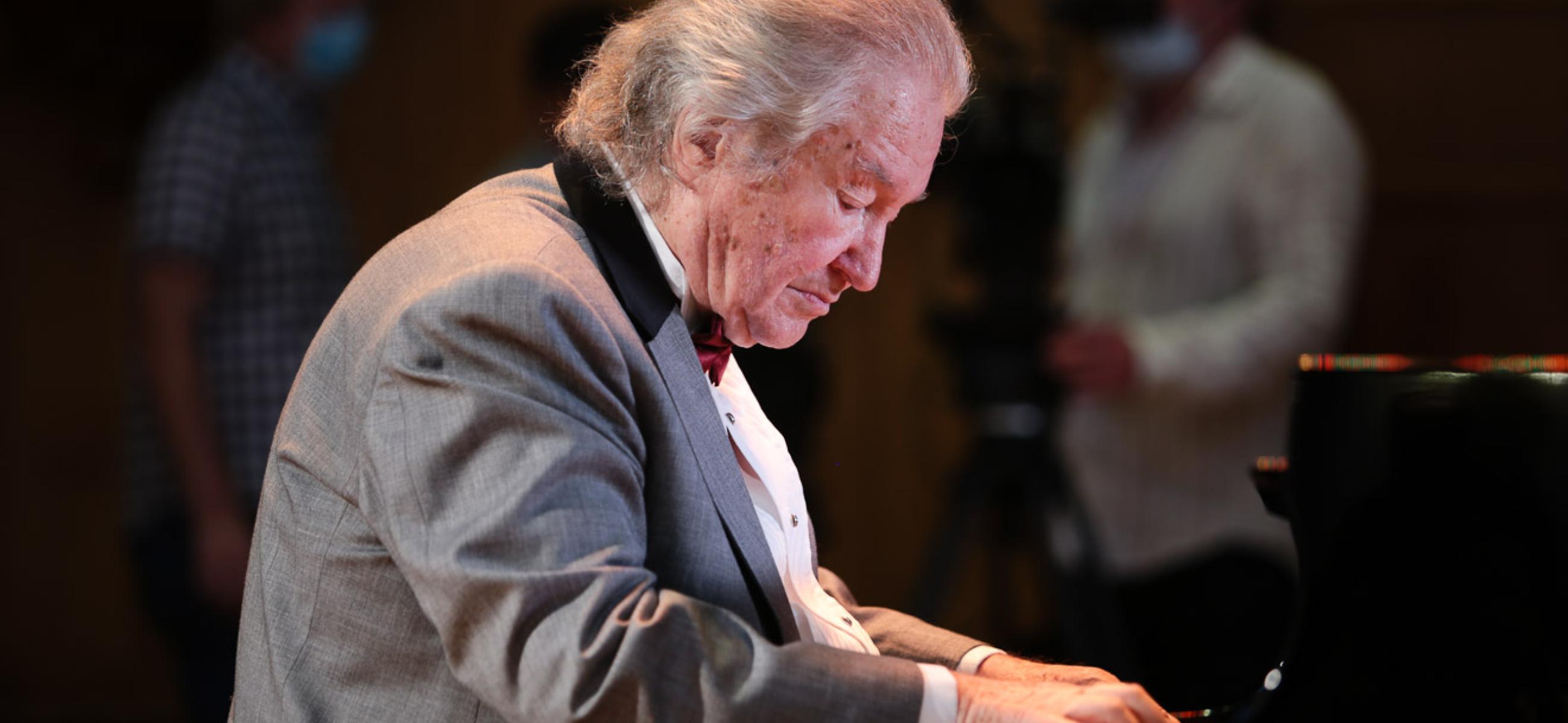 Mikhail Voskresensky in a gray suit, appears very focused while playing a piano.