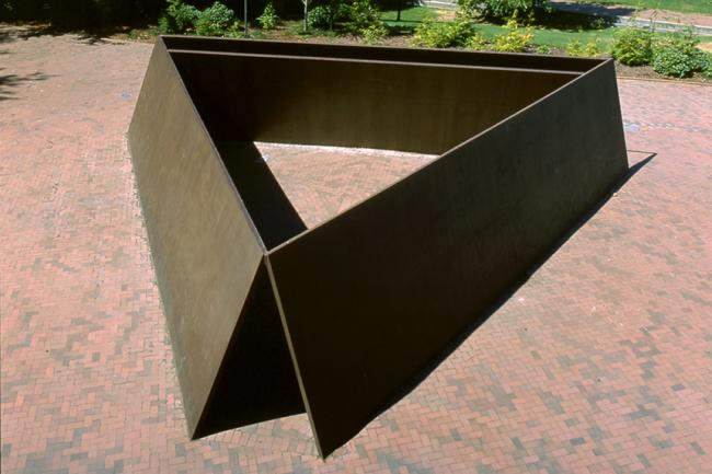 view from above: metal rectangular slabs standing with long edges on a brick plaza join together at the top corners to form a triangle which people can walk through.