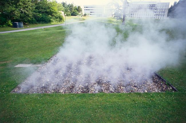 clouds of steam rising from a square pit of rocks in the lawn. A breeze gently spreading the steam to the right..