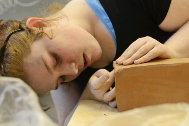 a student looks closely as they work on a corner of a clay brick