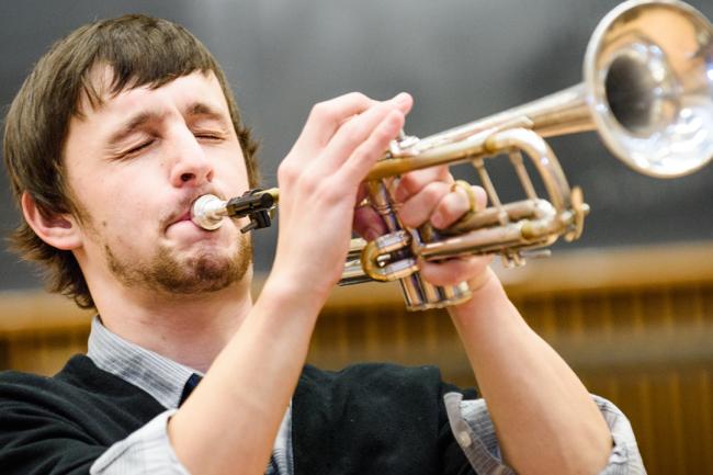 A person closing their eyes as they blow into a horn instrument