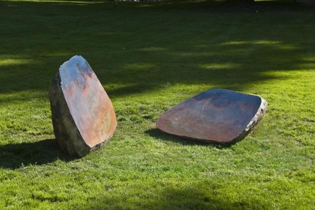 Two halves of a boulder on a lawn. The split sides are flat, polished, and portray a colorful, reflective surface.