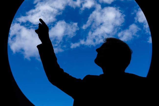 silhoutte of a person pointing up at clouds in a blue sky from inside a circle