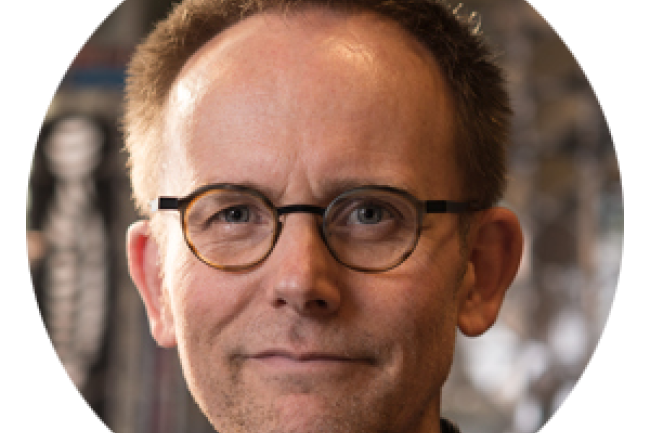 close-up of Dr. Craig Hella Johnson's face: short cropped hair, round glasses and a slight smirk