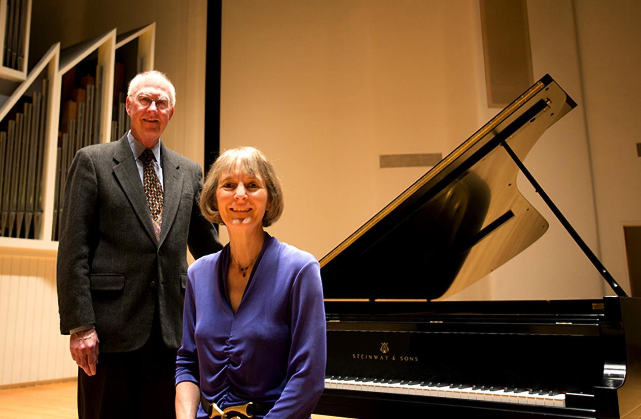 An elderly man and woman next to a Steinway piano, smiling