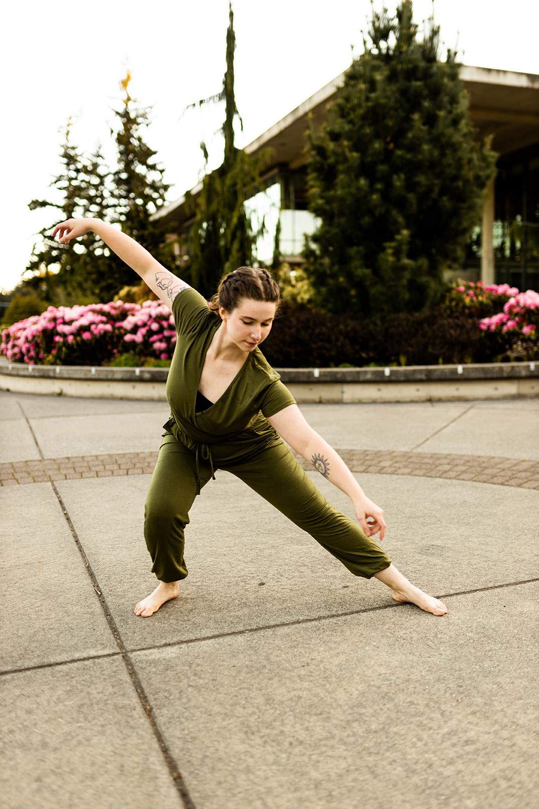 Chloe in a park setting, posing in a side lunge with one hand parallel to the outstretched leg and the other up in the air to form a straight line as she gazes at the ground