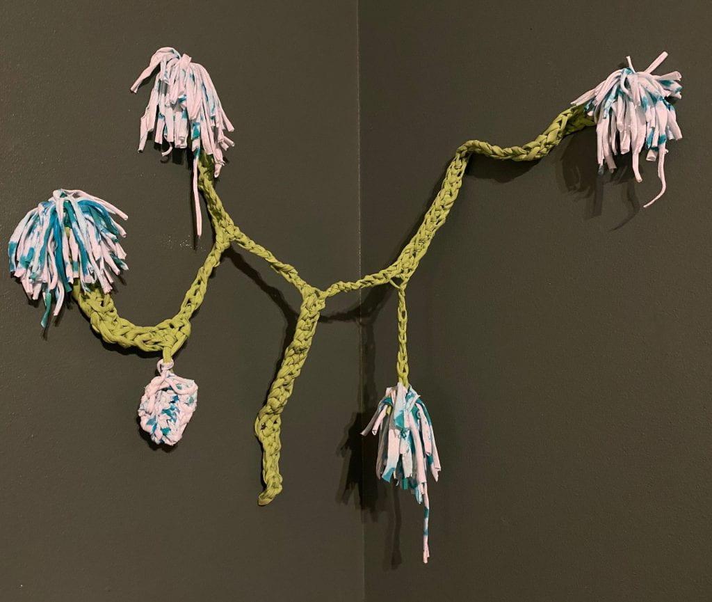 knitted strands and pompoms hang in a corner of the wall like a cartoon tree