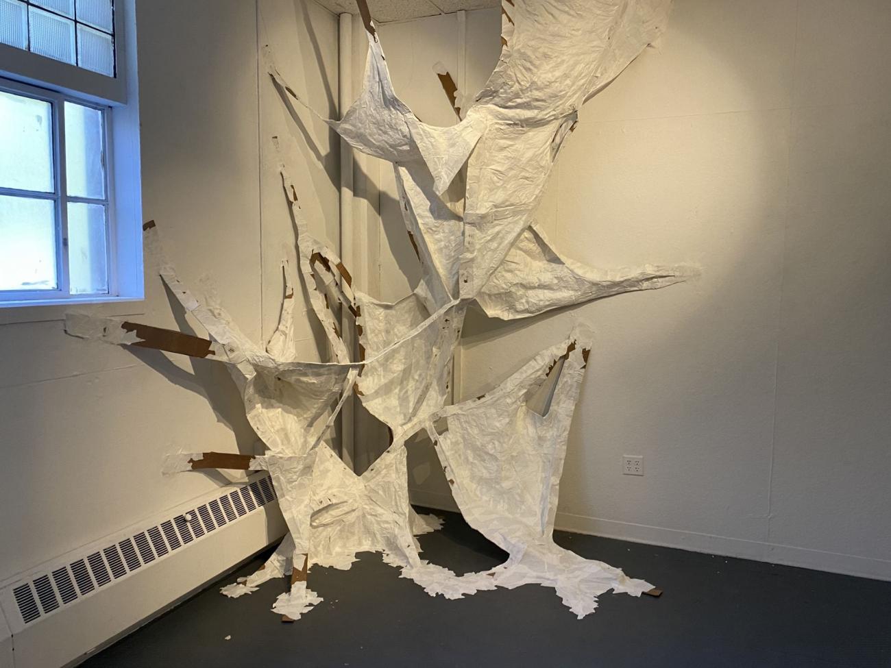 tattered white sheets of some lightweight material hang in the corner of a room like worn-out sails, connected by cardboard strips