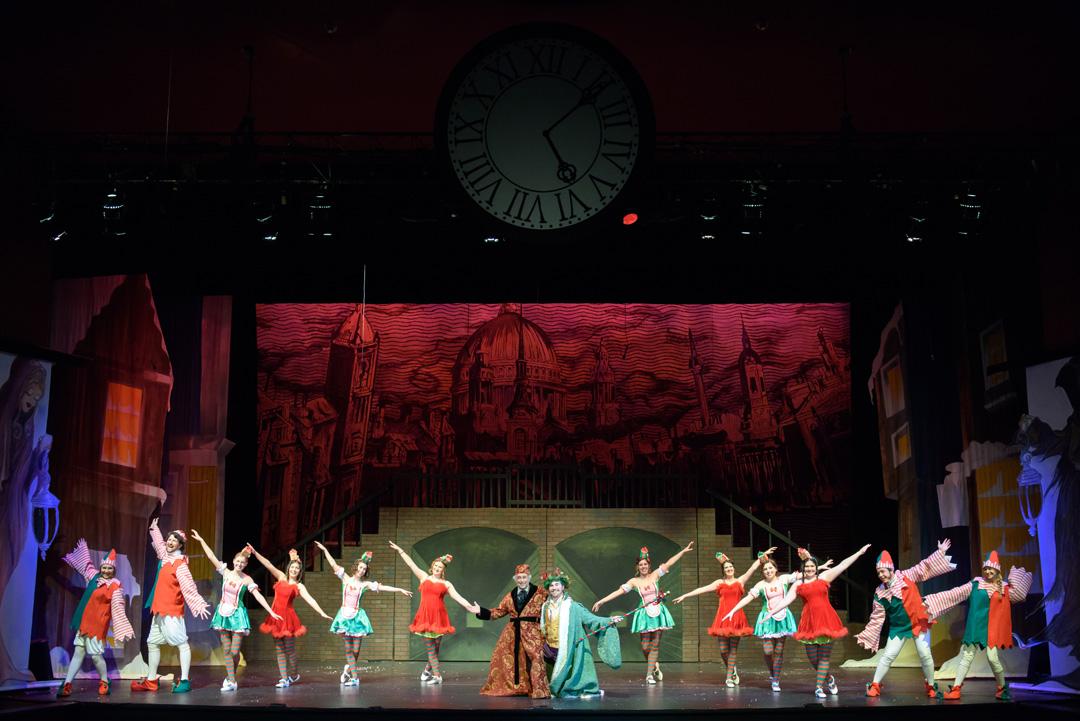 Dancers in Christmas apparel pose under a large analog clock.