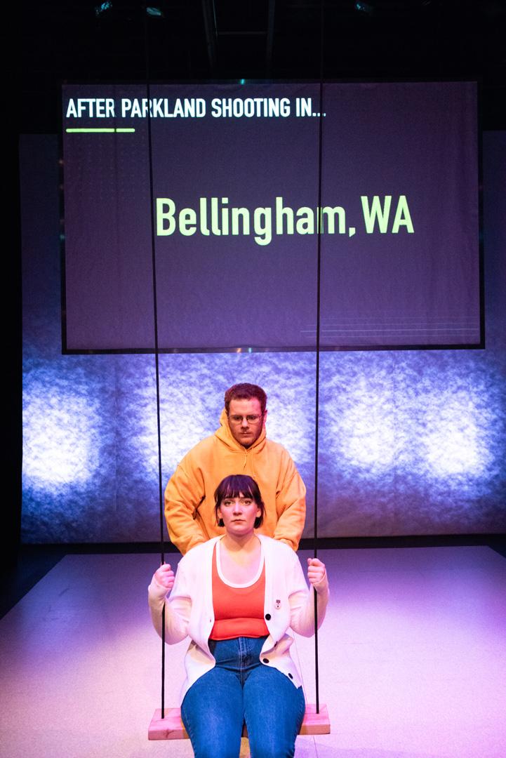 Actor pushes another on a swing both with dejected expressions as the screen behind reads "After Parkland Shooting in Bellingham, WA".