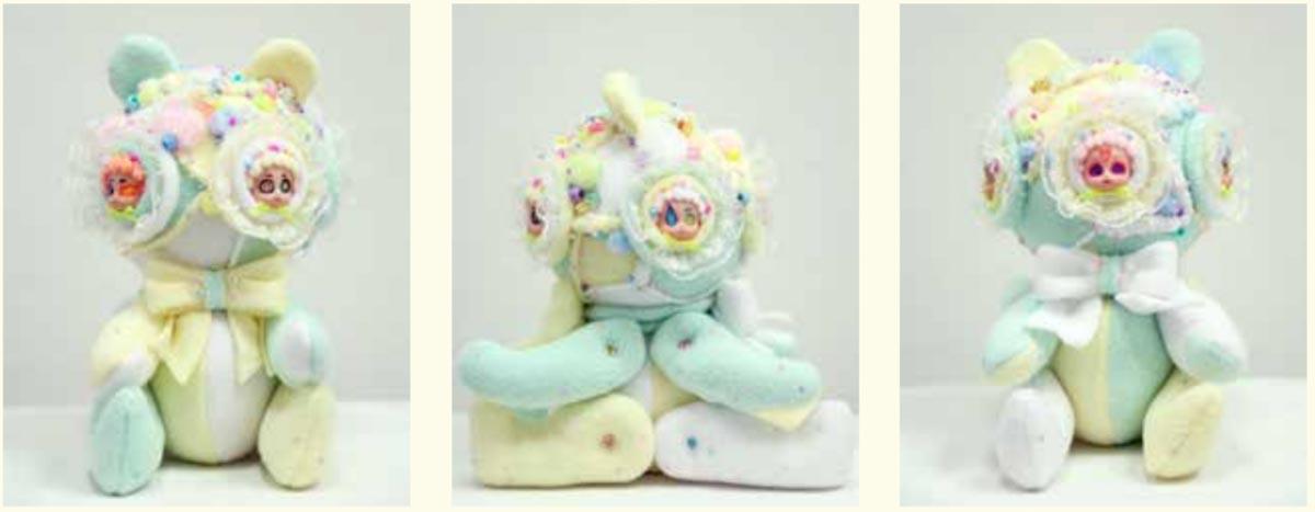 a pastel plush doll fused like a conjoined twin at the back to another one. Both have baby doll faces for their eyes.