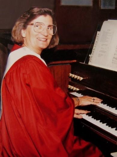 A woman in a ceremonial robe smiles while playing piano