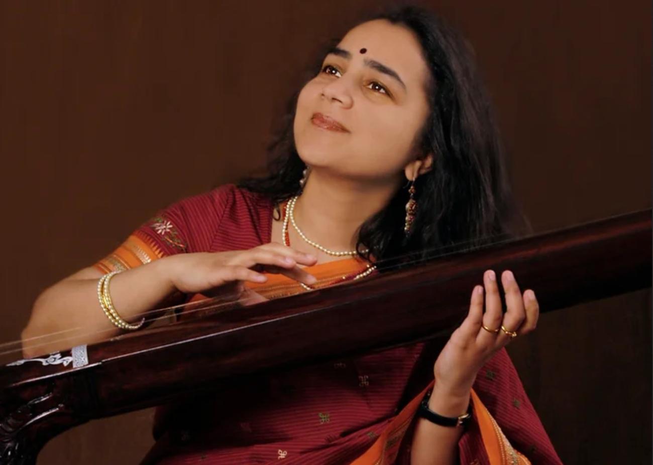 Srivani Jade holding a long Indian string instrument, looking up with a calm, blissful expression