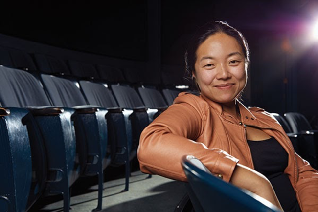 theatre director in tan leather jacket sitting in audience seats