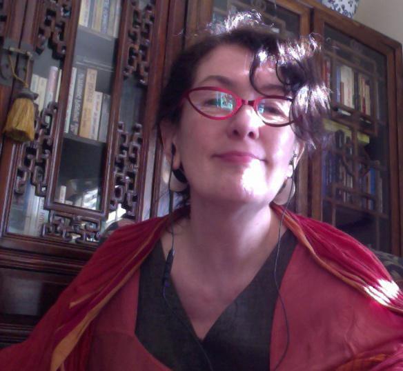 Beth Carruthers wearing cat-eye style glasses and a proud smile, sitting in front of an intricate antique bookcase