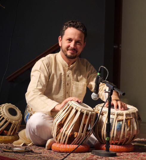 Ravi Albright sitting on the floor, playing Tabla in front of a microphone