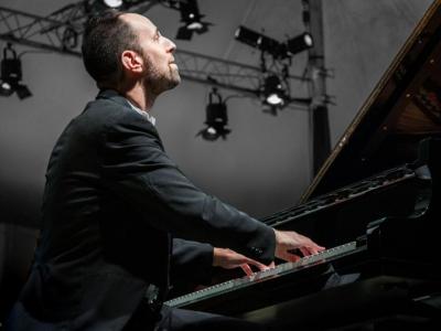 View from the side at floor level: Spencer Myer looks up dreamily as he plays the piano. Stage lights are visible high in the air behind him.