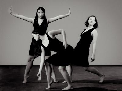 3 dancers posed: in front, a dancer bends at the knees and reaches down with one hand - one heel and the other elbow lifted up. To the right, a dancer bends at the knees in a partial lunge and leans back, letting their arms dangle. In the back, a dancer stands on toes with legs and arms spread into the shape of a star, and wrists bent so all fingers are pointed up.
