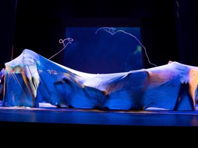 performers draped in diaphonous fabric in deep blue light 