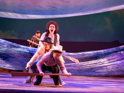 actors with boat paddles struggling through fabric suggestive of turbulent water
