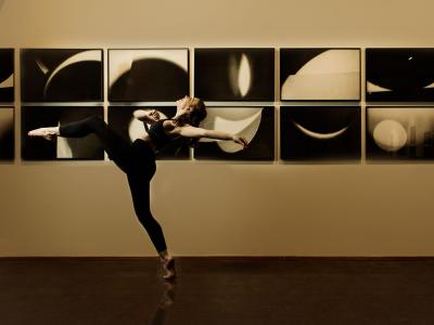 dancer takes an enormous step with back and arm arched back while passing a row of black and white abstract photos