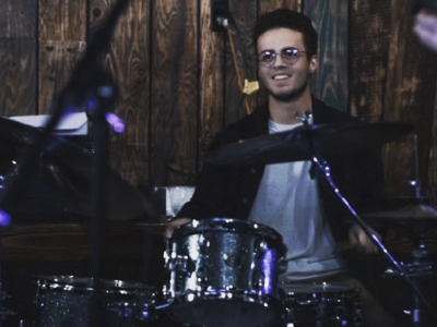 A happy person playing drums in front of a wood paneled wall