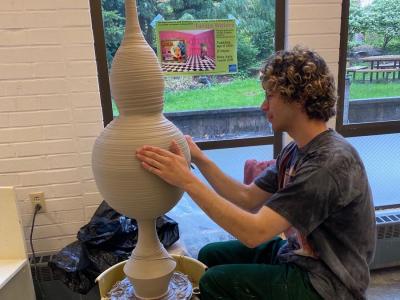 a person molds a clay urn on a pottery wheel