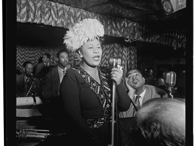 Ella Fiztgerald sings into a microphone in a black and white historical photo