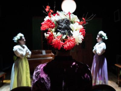 the back of a person's head with a wreath of flowers - in front of them two people appear rapt in prayer