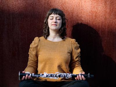 Rachel Yoder assumes a meditative pose with eyes closed, holding a clarinet horizontally across both open palms