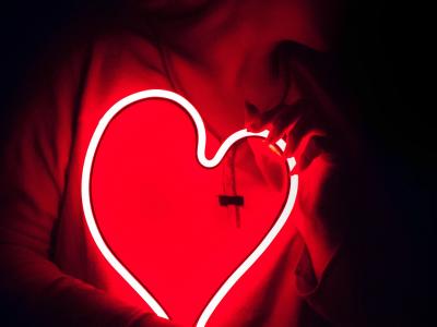 A person holding a neon heart close to their torso, bathed in red light from the heart
