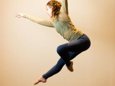 A dancer leaping, bent forward, hands stretched out, one leg bent toward the other, all toes pointed