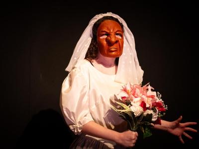 a masked performer in a veil holds flowers