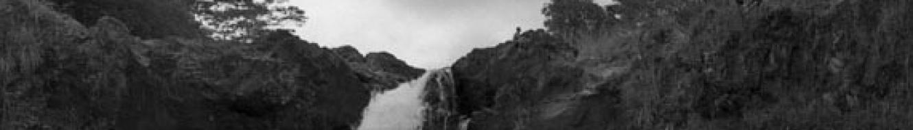 black and white photo of waterfall with pool and two people on shore in foreground